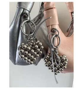 Detail of trendy ruched pouch bag featuring a metallic heart-shaped beaded charm accessory