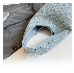 Detail of light blue denim shoulder bag featuring silver studs and wide strap