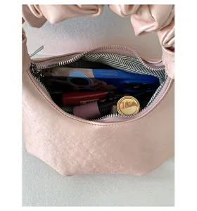 Detailed top view of pink ruched handbag showing zipper closure and herringbone lining