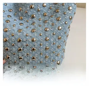 Macro detail of light blue denim fabric with silver rivets and distressed fringe edges