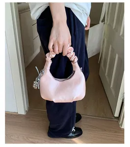 Detail of pink crescent bag with pleated handle and metallic sphere charm accessory