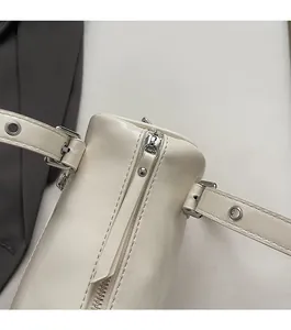 Detail view of the smooth silver metal zipper and adjustable strap eyelets on cream pillow bag