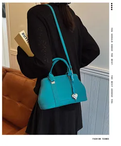 Detail of teal lychee grain leather handbag featuring silver heart charm and shoulder strap