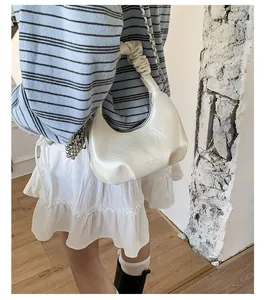 Close-up of white glossy hobo bag with ruched handle and elegant silver chain strap