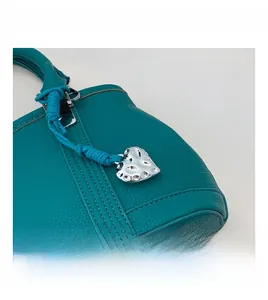 Close-up of turquoise lychee leather bag with silver heart charm and blue woven rope