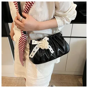 Detail of black glossy pleated bag with white bow and pearl charm on a model