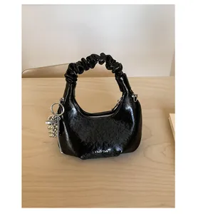Detail of black glossy pleated handbag featuring a silver beaded charm on a wooden surface