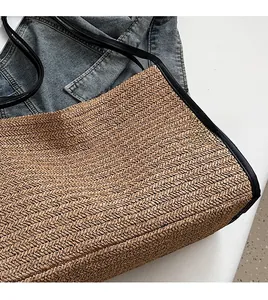 Close-up of brown woven straw tote bag featuring herringbone pattern and black leather strap