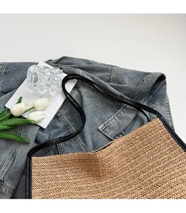 Detail of woven straw tote bag featuring black leather shoulder straps and natural texture