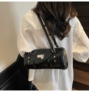 Détail du sac baguette cylindrique noir brillant avec boucles argentées sur chemise