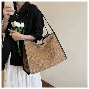 Detail of woven straw tote bag with black leather straps on model shoulder