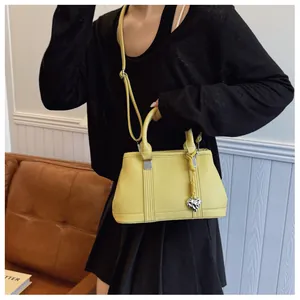 Detail of yellow lychee texture handbag featuring a silver heart charm and adjustable strap