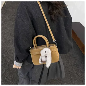 Outdoor shot of a light brown crossbody bag with a cute plush rabbit charm detail