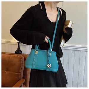 Close-up of litchi grain texture on teal crossbody bag with heart-shaped metal pendant