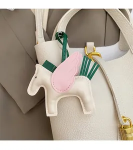Detail of a handmade leather Pegasus bag charm with pink wings on a white bucket bag