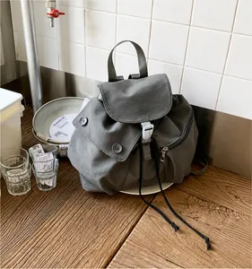 Detail view of dark grey nylon backpack with drawstring and magnetic buttons on wooden table