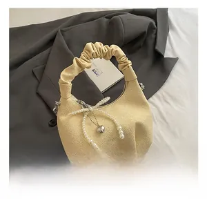 Detail of light yellow woven crescent bag with pearl bow and silver heart pendant