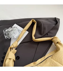Detail of cream pleated leather bag with knotted wide shoulder strap on blazer background