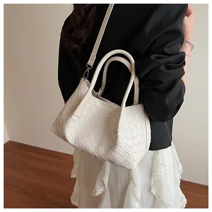 Détail du sac seau en cuir tressé crème avec bandoulière réglable porté à l'épaule