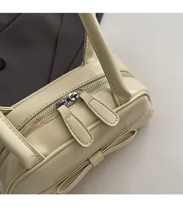 Detailed view of dual smooth zipper closure and bow accent on beige shoulder bag
