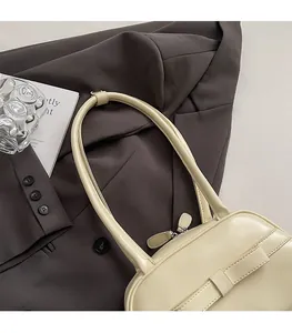 Detail of creamy white PU leather bowling bag with bow decoration on a brown blazer