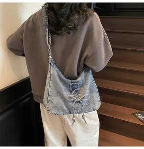 Détail du sac bandoulière en denim délavé avec nœuds et garnitures métalliques sur un mannequin