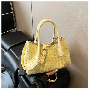 Détail d'un sac seau en cuir tressé jaune clair avec motif en croix et anses rondes