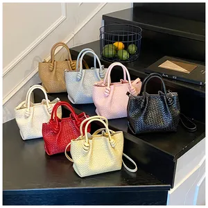 Close-up of seven assorted woven bucket bags in various colors on black wooden stairs