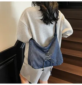 Détail du sac bandoulière en denim bleu avec laçage décoratif et perles métalliques