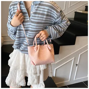 Pink woven bucket bag with knot handle and crossbody strap, styled on model for summer outfit