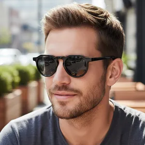 Modern oval black frame sunglasses with dark lenses worn by a model in outdoor lighting
