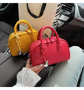 Detailed close-up of mini Boston bags in yellow and red lychee grain leather with bell charm