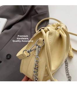 Detail of creamy drawstring bucket bag showing pleated texture and silver chain strap