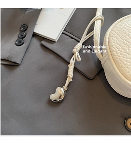 Detail of silver heart metal pendant with ivory woven rope on a textured handbag