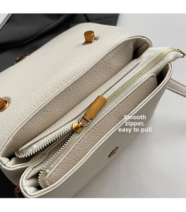Détail de la fermeture éclair dorée et du cuir grainé sur un sac à bandoulière beige