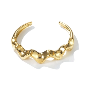 Close-up of a wavy gold cuff bracelet with a polished mirror finish and open design