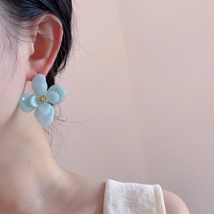 Détail de boucles d'oreilles fleur en acrylique bleu clair portées par un mannequin