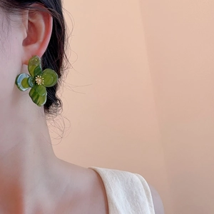 Détail de boucles d'oreilles fleurs en acrylique vert avec ornements dorés centraux