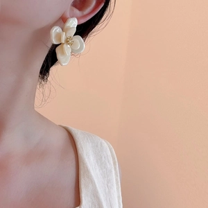 Détail d'une boucle d'oreille fleur en acrylique blanc crème avec centre doré sur l'oreille