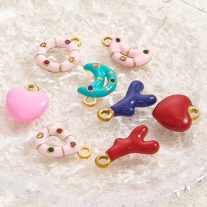 Detail of colorful enamel heart and moon charms with zircon inlays on a textured tray