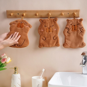 Close-up of three cute cartoon brown capybara hand towels hanging on wooden hooks in a bathroom