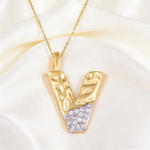 Macro shot of letter V pendant with hammered gold texture and pave-set zircons on white silk