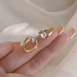 Détail de boucles d'oreilles dorées torsadées avec un zircon rond sur satin beige