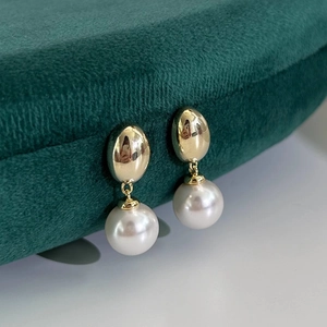 Detailed side view of elegant pearl drop earrings on a dark green velvet display stand