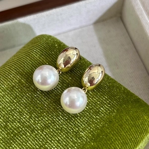 Detailed close-up of gold oval studs with round white pearls on green velvet