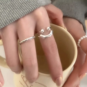 Detail of s925 silver smiley face open ring set on a hand holding a ceramic mug