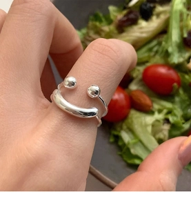Detail of s925 silver smiley face layered ring worn by model with fresh salad background