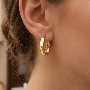 Elegant gold hexagon hoop earrings worn by a model in warm indoor natural lighting
