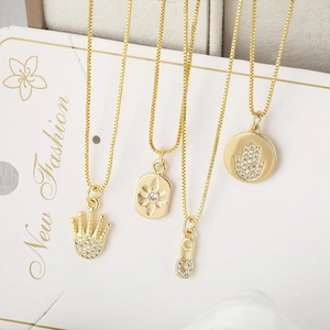 Détail de colliers plaqués or avec main de hamsa, couronne et pendentifs soleil