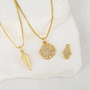 Pendentifs Hamsa et pointe en or sur chaînes gourmettes sur fond de pierre blanche texturée